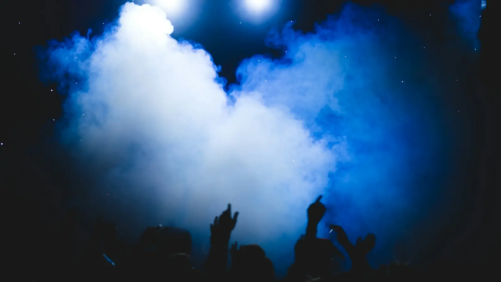 Thick cloud of fog lit by blue stage lights above a crowd