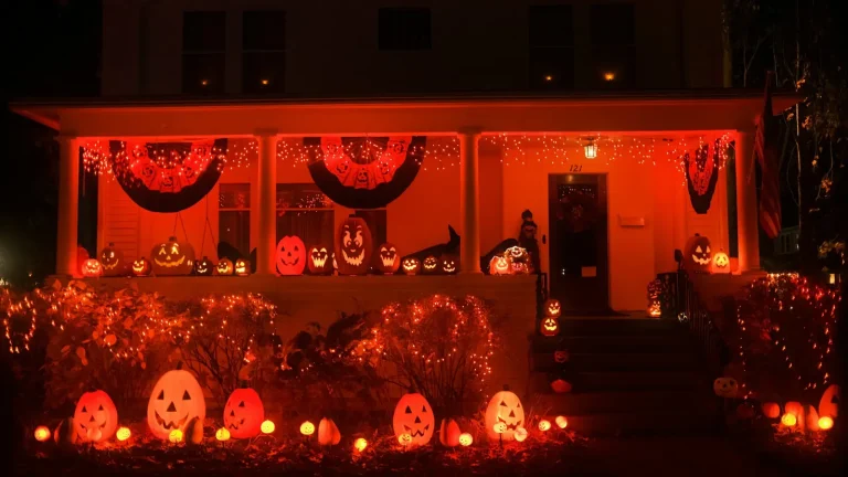House porch covered in orange Halloween lights and glowing pumpkins at night