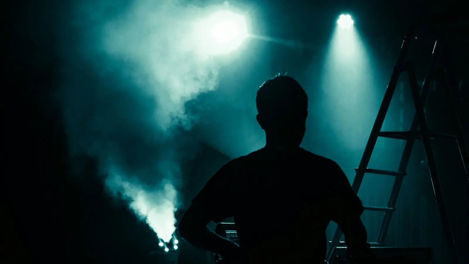 Silhouette of a person in front of stage fog and teal spotlights