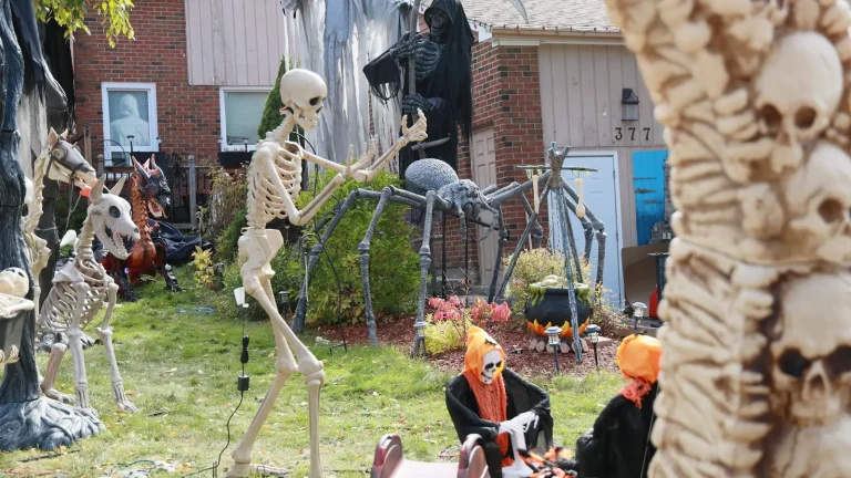 Front-yard Halloween display with posed skeletons, a giant spider and grim reapers